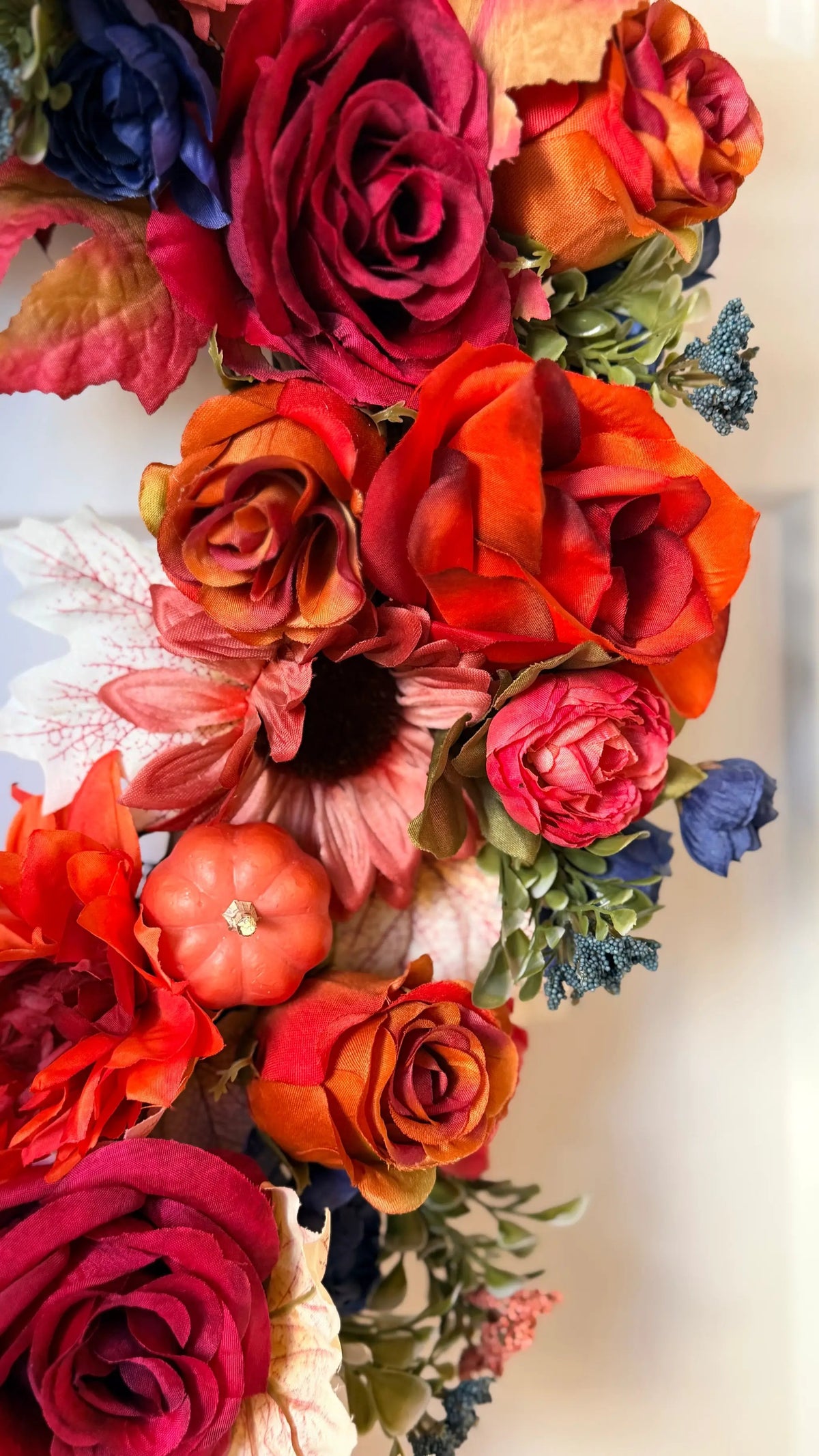 Vibrant fall wreath featuring orange roses, sunflowers, maple leaves, and a small pumpkin in rich autumn colors.