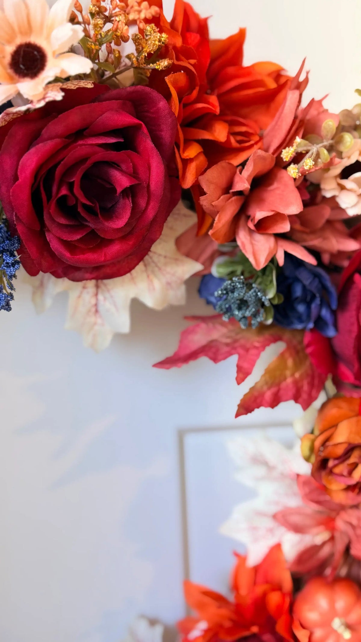 Vibrant fall wreath featuring deep red roses, orange blooms, and autumn leaves for seasonal home decor.