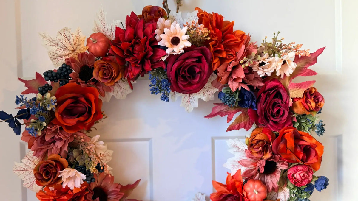 Vibrant Fall wreath featuring red and orange roses, autumn leaves, pumpkins, and blue berries on a white door.